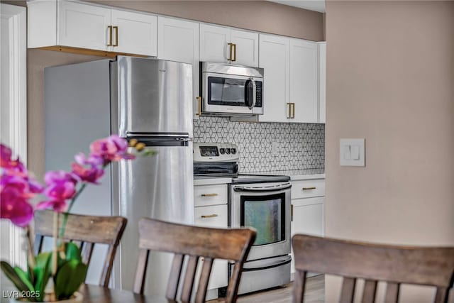 kitchen with appliances with stainless steel finishes, light wood-style flooring, backsplash, and white cabinetry