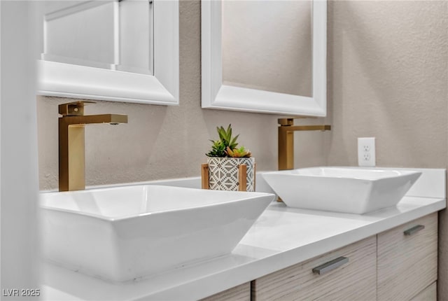 bathroom featuring a textured wall, double vanity, and a sink