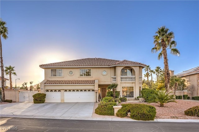 mediterranean / spanish home with stucco siding, concrete driveway, an attached garage, a balcony, and a tiled roof