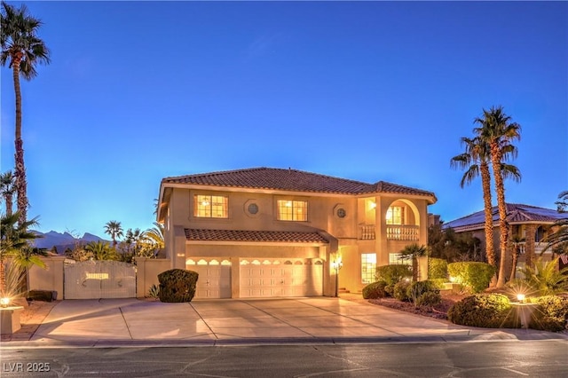 mediterranean / spanish-style home with a gate, stucco siding, concrete driveway, a garage, and a tiled roof