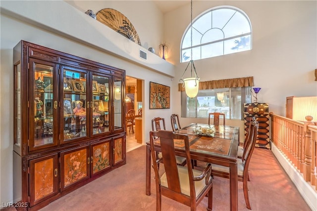 carpeted dining space with visible vents and a towering ceiling