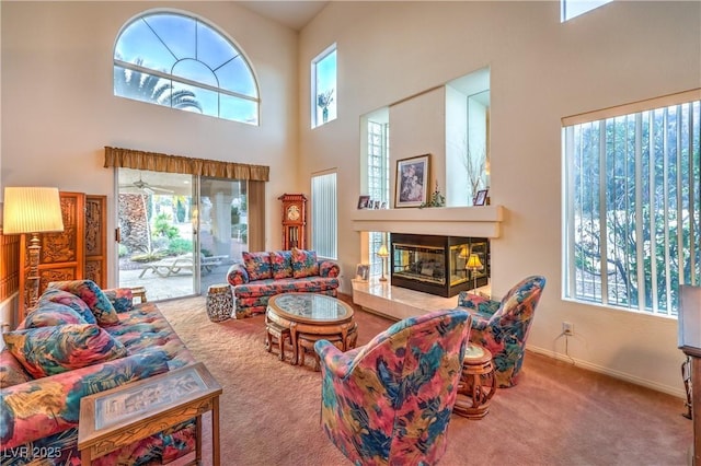 living room featuring carpet, a healthy amount of sunlight, a towering ceiling, and a tiled fireplace