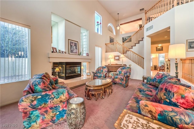 living area featuring stairway, visible vents, carpet floors, a high ceiling, and a glass covered fireplace