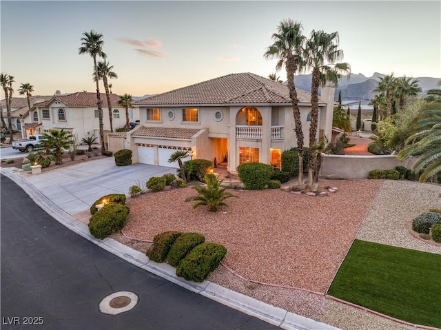 mediterranean / spanish home featuring a tiled roof, stucco siding, a garage, a balcony, and driveway