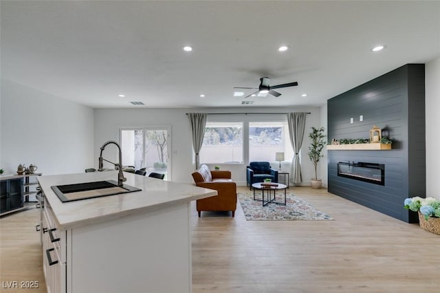 kitchen with open floor plan, recessed lighting, light wood-style flooring, a fireplace, and a sink