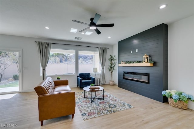 living area with a large fireplace, visible vents, light wood-style floors, and recessed lighting