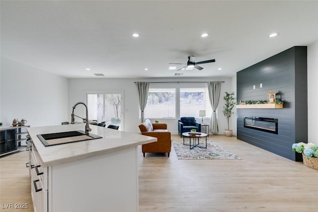 kitchen with light wood-style flooring, a sink, open floor plan, white cabinetry, and a fireplace