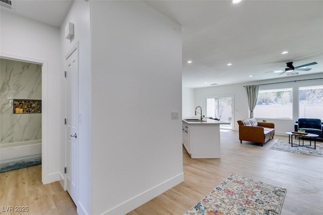 hall with recessed lighting, light wood-style flooring, baseboards, and a sink