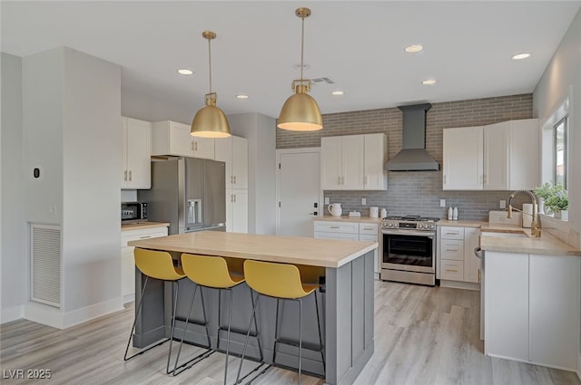 kitchen featuring stainless steel appliances, visible vents, a sink, wall chimney range hood, and a kitchen island