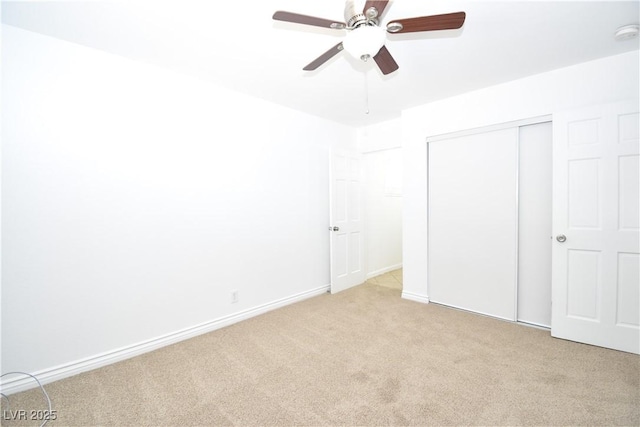 unfurnished bedroom with light carpet, a closet, a ceiling fan, and baseboards