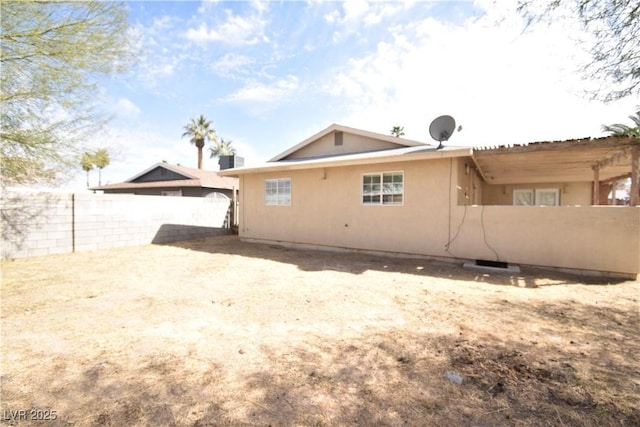 rear view of house featuring fence and stucco siding