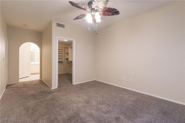 unfurnished bedroom featuring carpet floors, arched walkways, a closet, visible vents, and a spacious closet