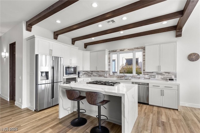 kitchen featuring visible vents, a center island, light stone countertops, stainless steel appliances, and a sink