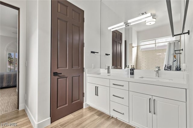 ensuite bathroom with double vanity, a sink, and wood finished floors