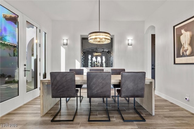 dining room with arched walkways, french doors, baseboards, and wood finished floors