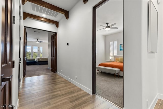 hallway featuring light wood finished floors, beamed ceiling, visible vents, and baseboards