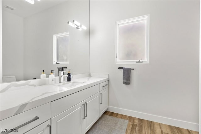 bathroom featuring toilet, wood finished floors, vanity, visible vents, and baseboards