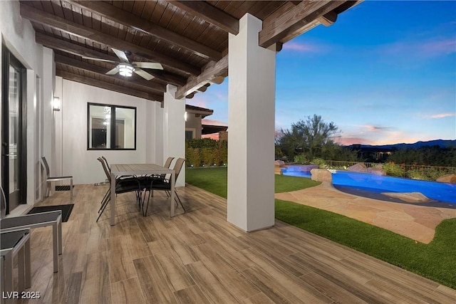 patio terrace at dusk featuring a fenced in pool, outdoor dining area, and a ceiling fan