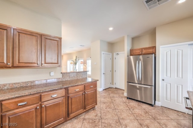 1332 Cedar Berry Ct, Henderson, NV 89012 - kitchen featuring freestanding refrigerator, brown cabinetry, light tile patterned floors, baseboards, and light stone countertops