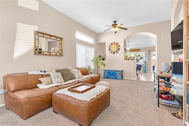 living area featuring carpet floors, baseboards, arched walkways, and a ceiling fan