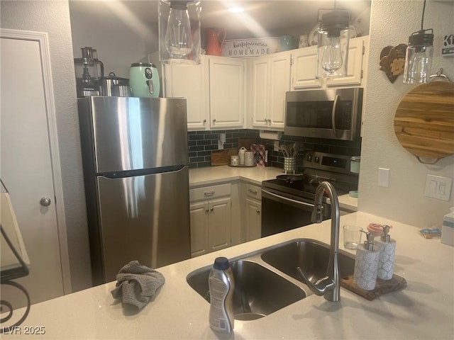 kitchen featuring white cabinets, decorative backsplash, stainless steel appliances, light countertops, and a sink