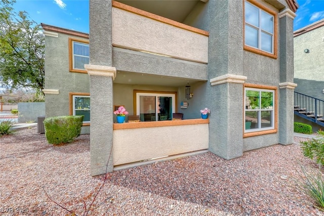 back of house with a fenced front yard, central air condition unit, stairs, and stucco siding