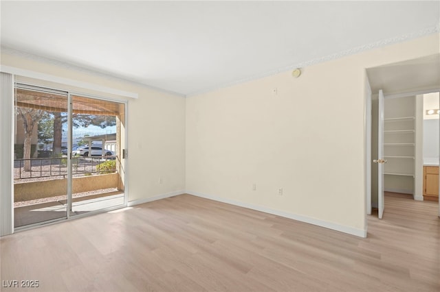 empty room with baseboards, crown molding, and light wood finished floors