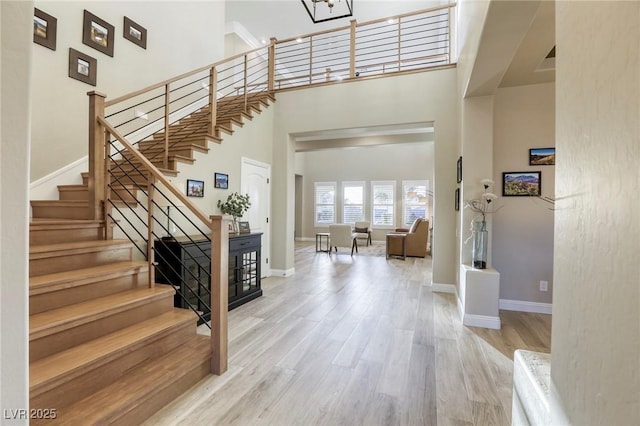 entrance foyer with stairway, a towering ceiling, baseboards, and wood finished floors