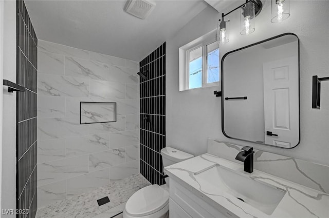 bathroom with toilet, visible vents, a tile shower, and vanity