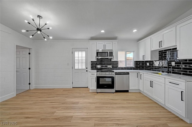 kitchen with light wood finished floors, stainless steel appliances, decorative backsplash, white cabinets, and a sink