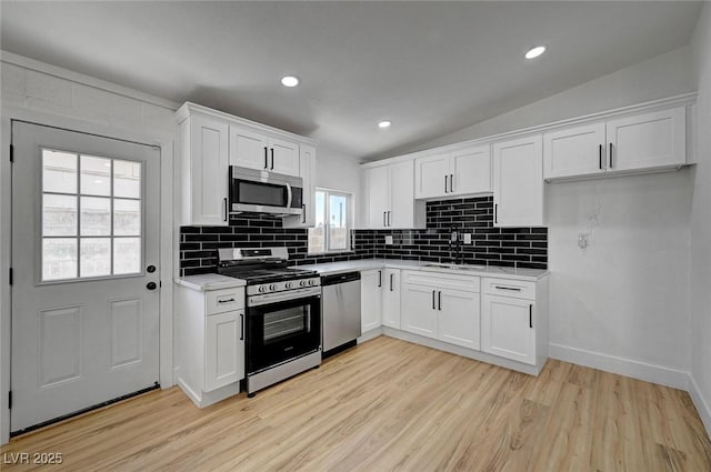 kitchen with lofted ceiling, stainless steel appliances, a sink, white cabinets, and light countertops