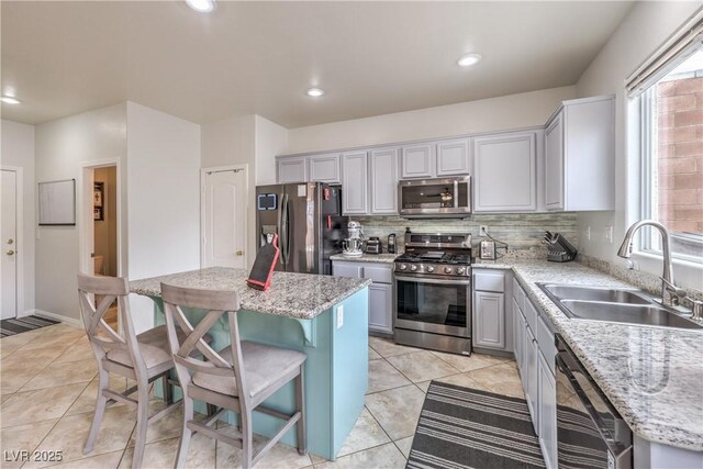 kitchen with a kitchen island, a sink, appliances with stainless steel finishes, gray cabinets, and tasteful backsplash