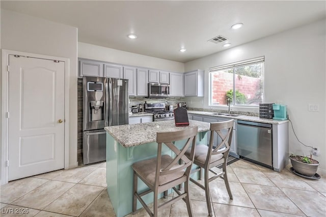 kitchen featuring light stone counters, stainless steel appliances, a sink, visible vents, and tasteful backsplash