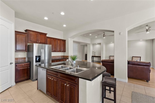 kitchen featuring arched walkways, dark countertops, open floor plan, stainless steel appliances, and a sink