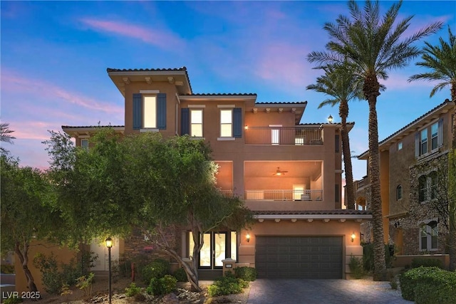 mediterranean / spanish house with decorative driveway, a tile roof, stucco siding, a balcony, and a garage