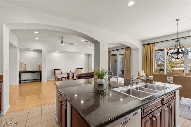 kitchen featuring light tile patterned floors, a center island with sink, arched walkways, a sink, and ceiling fan with notable chandelier