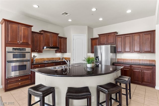 kitchen with light tile patterned floors, a breakfast bar, stainless steel appliances, under cabinet range hood, and a sink