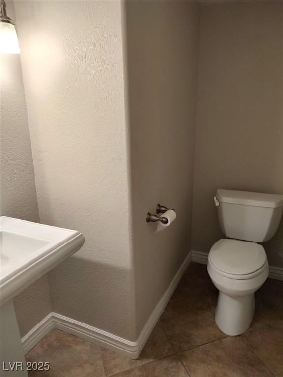 bathroom with toilet, tile patterned flooring, baseboards, and a sink