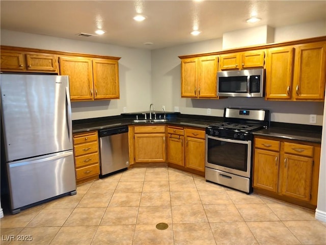 kitchen featuring stainless steel appliances, brown cabinetry, dark countertops, and a sink