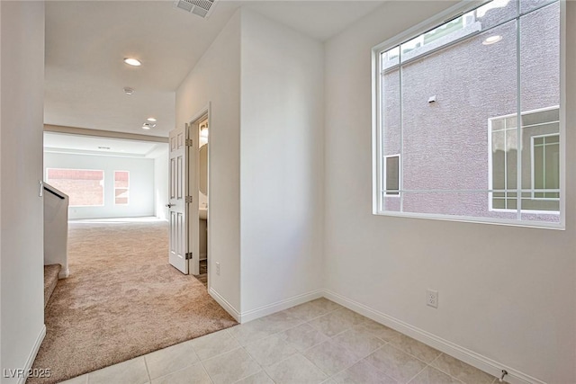 corridor with light carpet, light tile patterned floors, baseboards, visible vents, and stairs