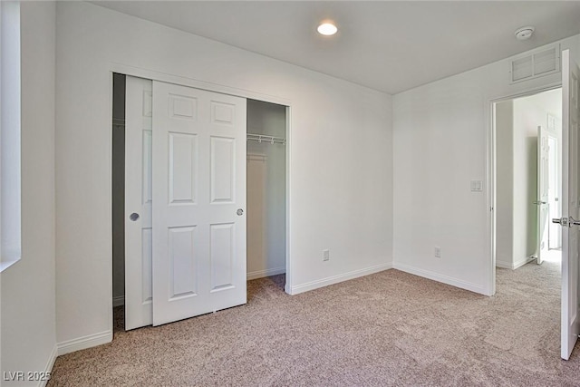 unfurnished bedroom with a closet, light colored carpet, visible vents, and baseboards