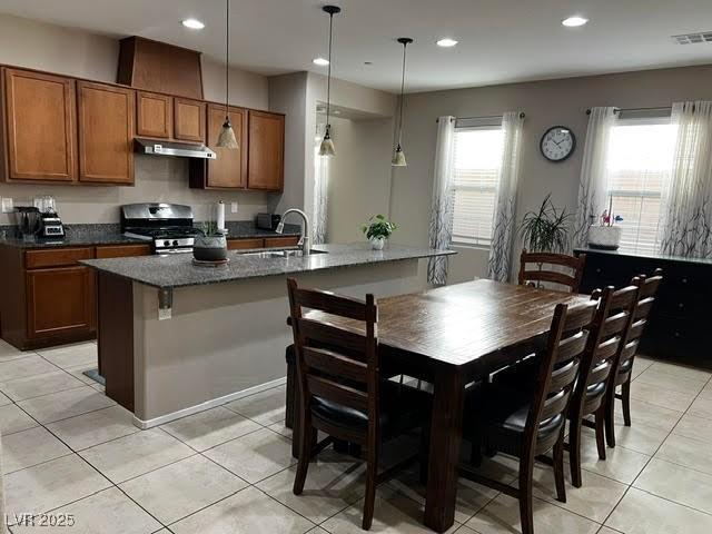 kitchen featuring under cabinet range hood, a sink, visible vents, brown cabinets, and stainless steel gas stove