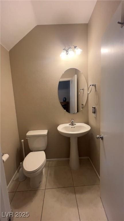 bathroom with lofted ceiling, baseboards, tile patterned flooring, and toilet