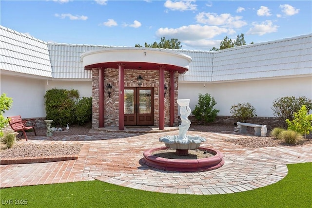 doorway to property featuring french doors, a tile roof, brick siding, mansard roof, and stucco siding