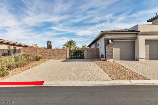 view of side of home featuring decorative driveway, stucco siding, an attached garage, and a gate