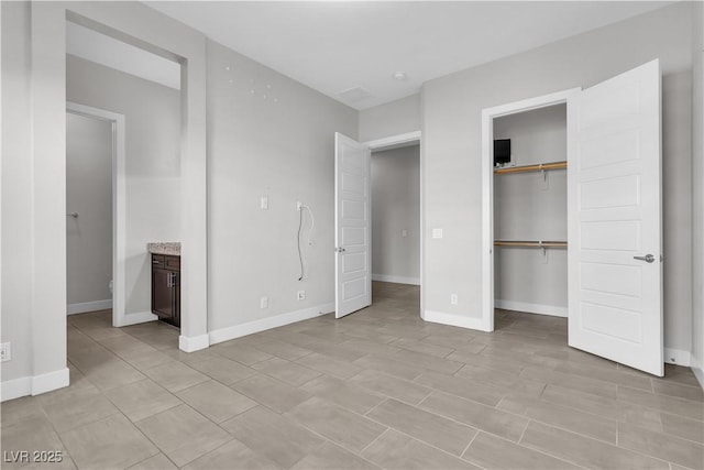 unfurnished bedroom with a closet, ensuite bath, and baseboards