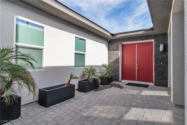 view of exterior entry featuring stone siding, a patio area, and stucco siding