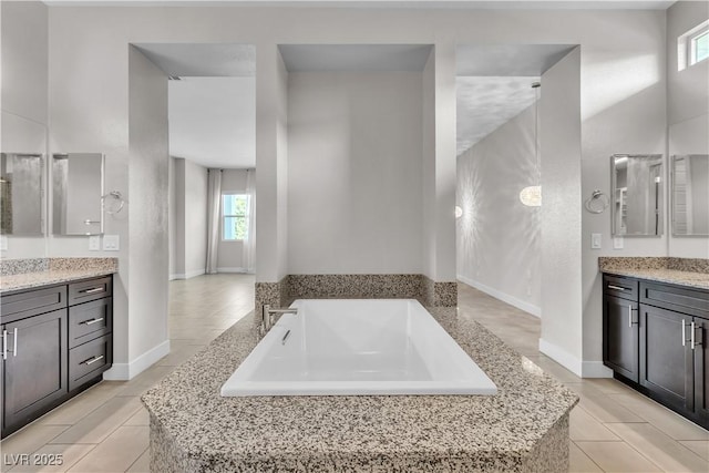 bathroom featuring tile patterned floors, baseboards, a bath, and vanity