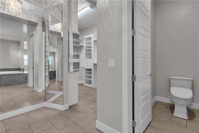 bathroom featuring baseboards, toilet, a bath, tile patterned flooring, and a closet