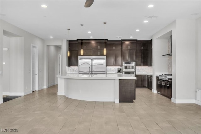 kitchen with a center island with sink, light countertops, backsplash, appliances with stainless steel finishes, and dark brown cabinetry